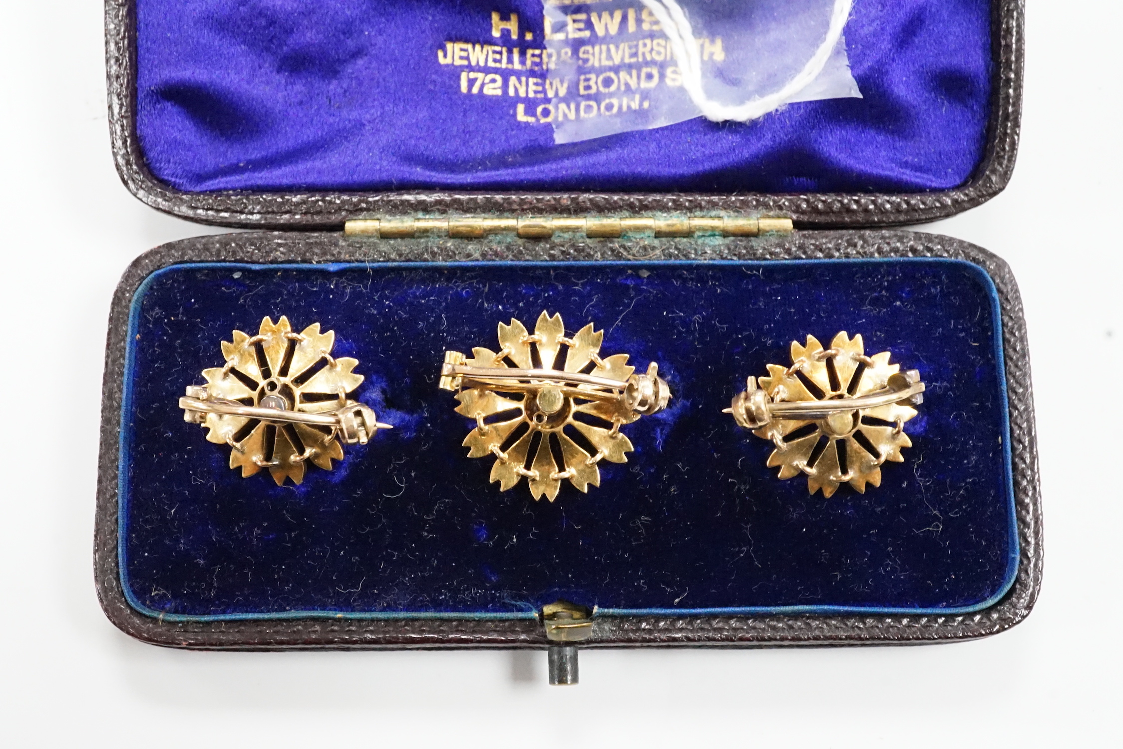A cased graduated set of three Edwardian yellow metal, seed pearl and diamond set flower head brooches, largest diameter 18mm, gross weight 10.9 grams.